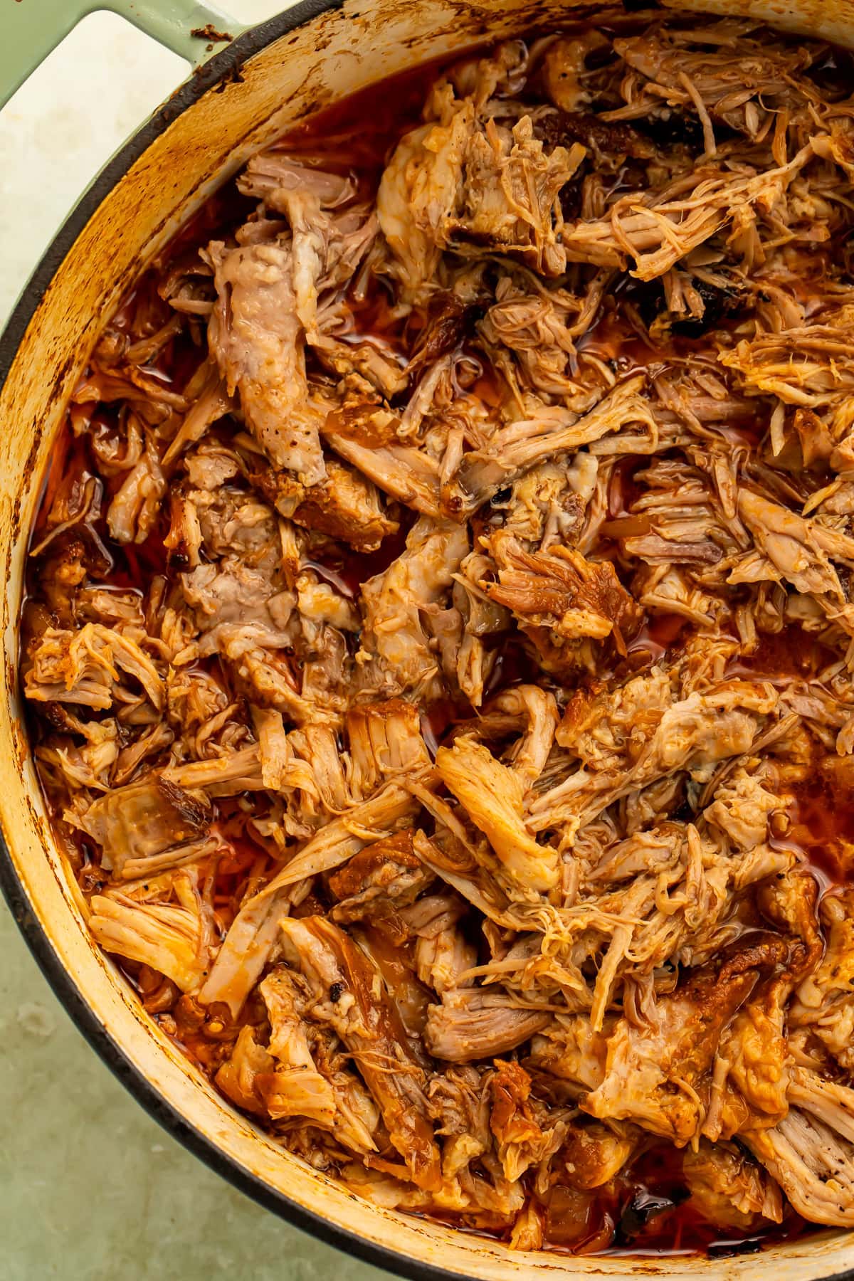 Close-up of juicy shredded chipotle braised pork in flavorful braising liquid.