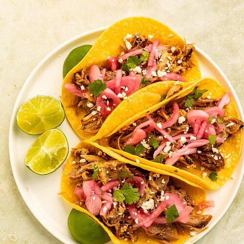 Chipotle pulled pork street tacos topped with pickled red onions, cotija cheese, cilantro, and fresh lime.