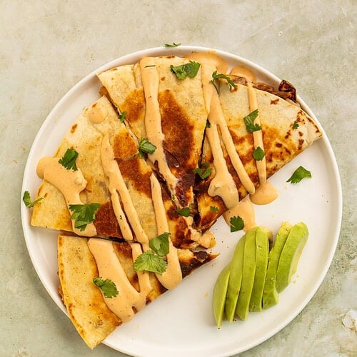 Loaded pulled pork quesadillas with chipotle crema, avocado slices, and fresh cilantro.