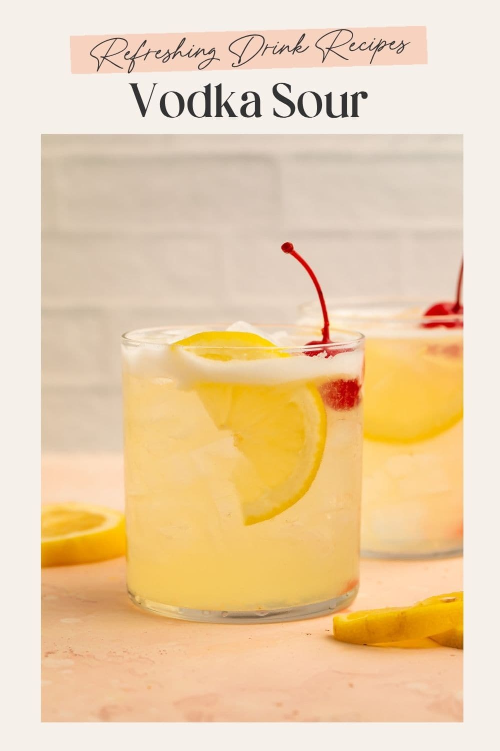 Two vodka sours with lemon slices and cocktail cherries on a pink countertop. The frame on the image has Pinterest-optimised text.
