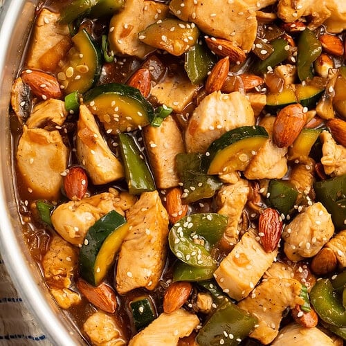 Close up of a chicken and almond stir fry with bell peppers and zucchini in a thick sauce.