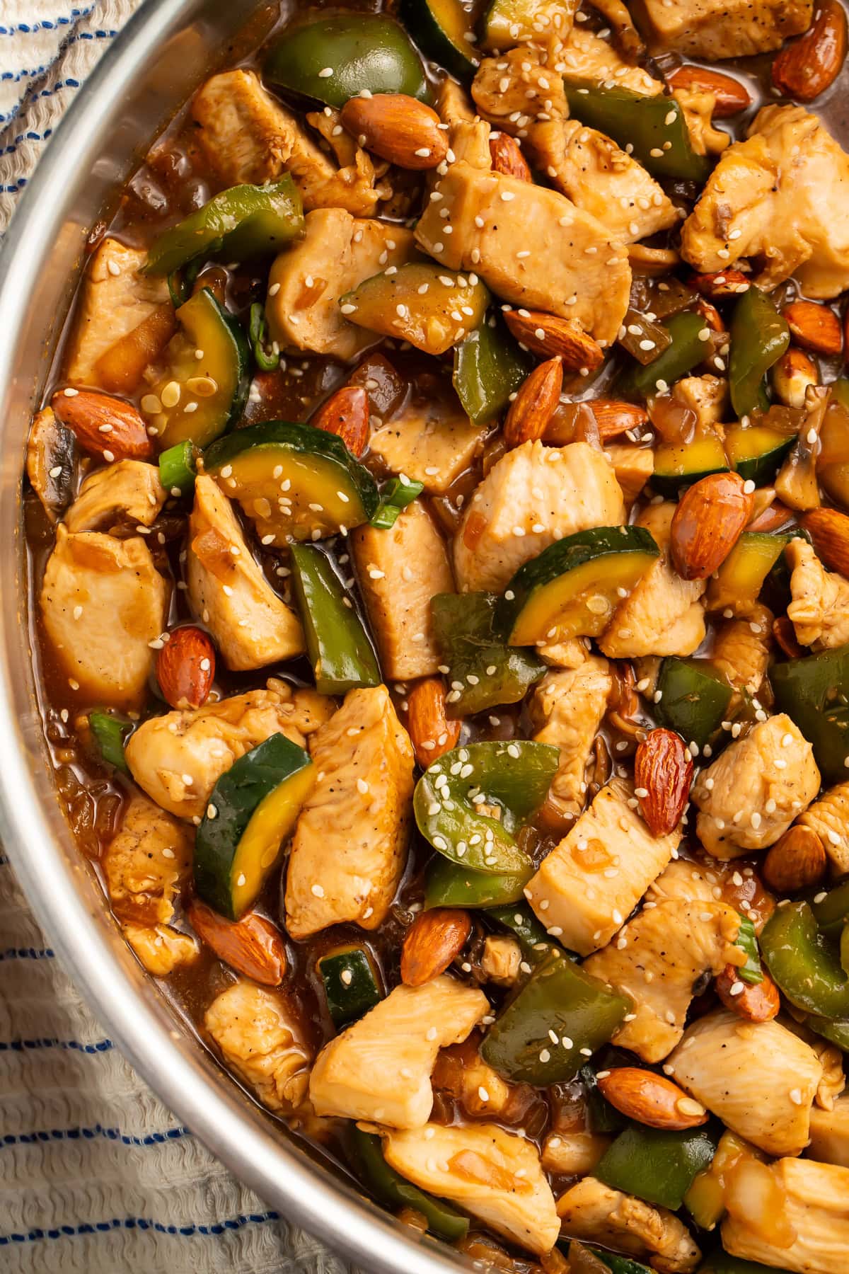 Close up of a chicken and almond stir fry with bell peppers and zucchini in a thick sauce.