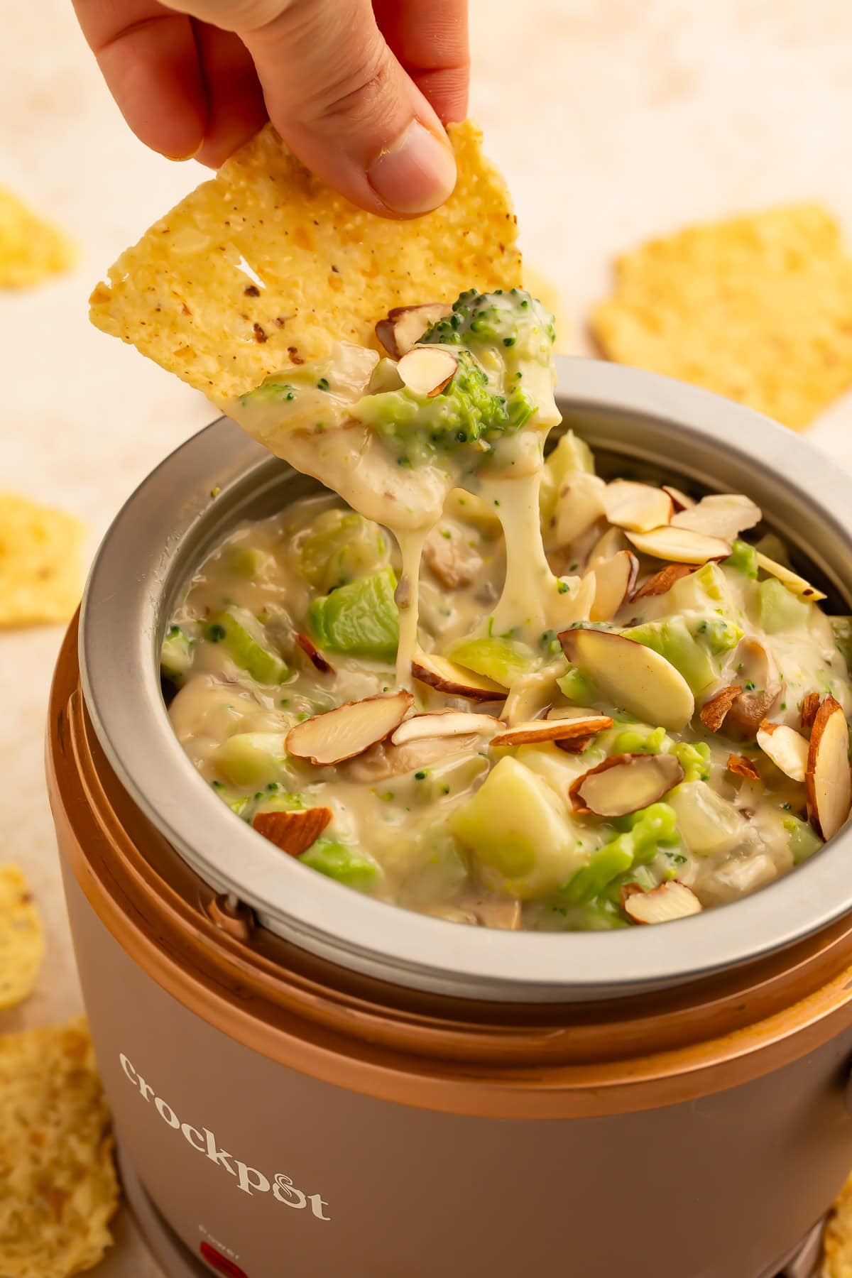 Hand with a tortilla chip scooping broccoli dip out of a mini crockpot.