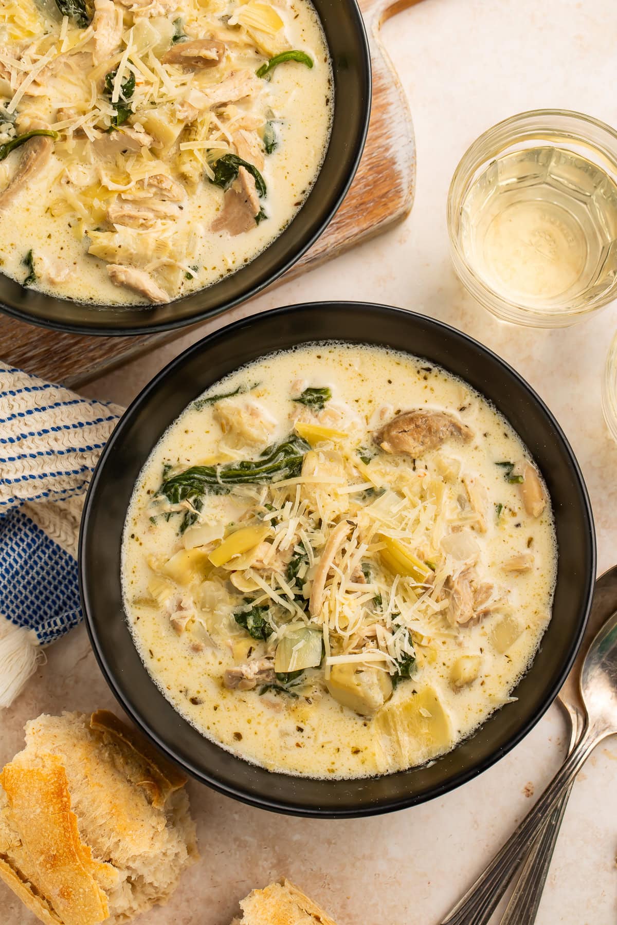 Two black bowls of chicken and artichoke soup topped with shredded cheese.