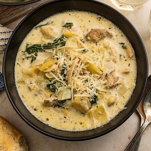 Close up of a black bowl of creamy chicken, artichoke and spinach soup.