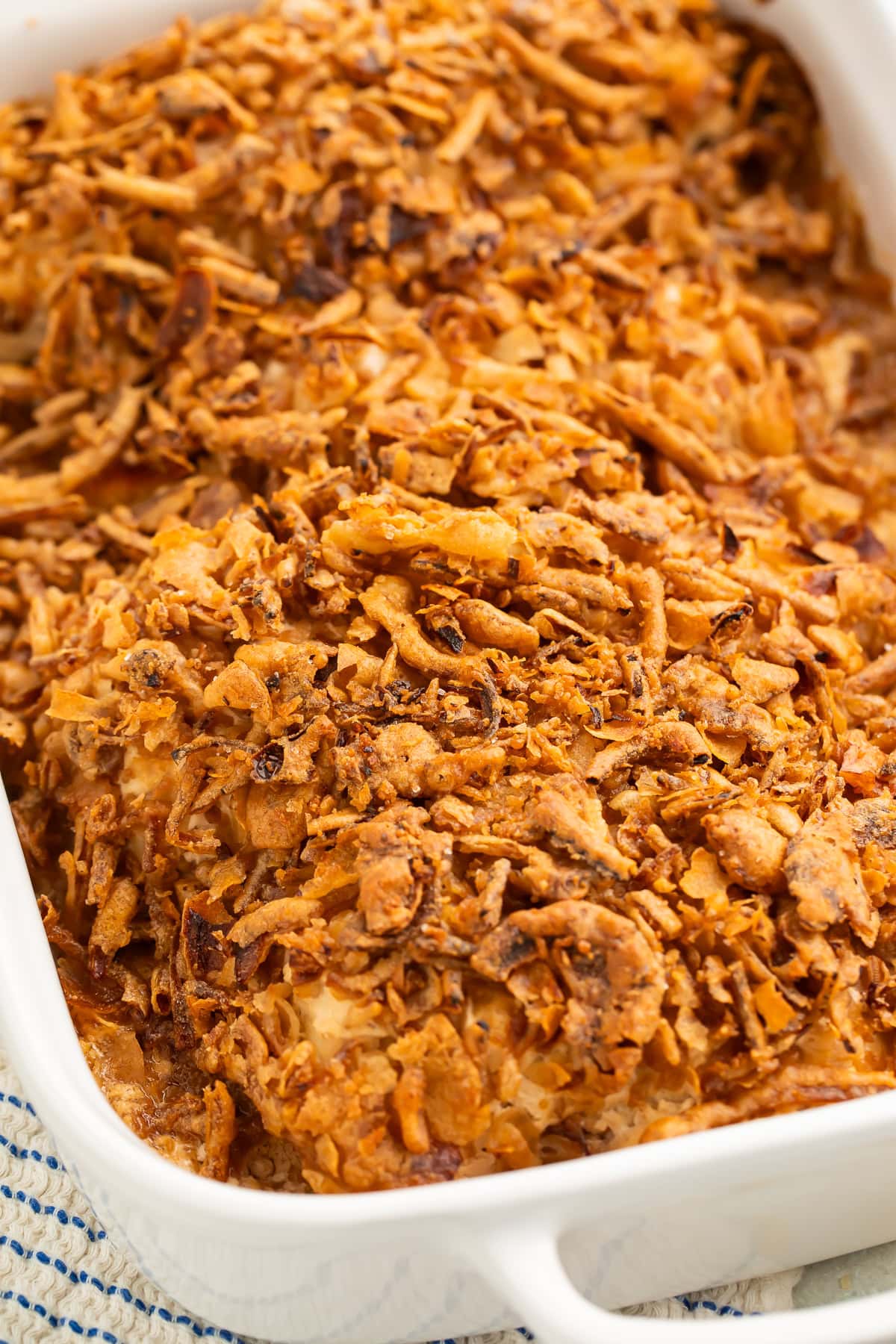 Close up of chicken breasts baking in a white baking dish smothered with crispy fried onions.