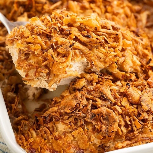 Close up of a chicken breast in a French onion bake with crispy onions being lifted out of a white baking dish.