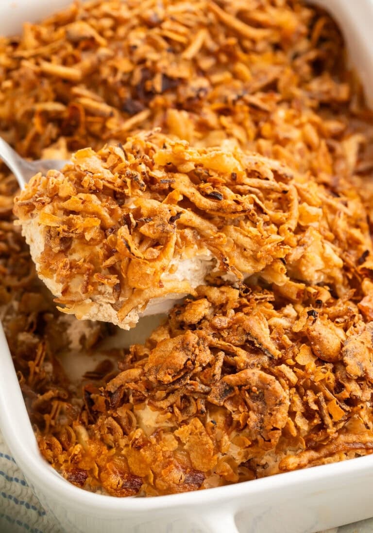 Close up of a chicken breast in a French onion bake with crispy onions being lifted out of a white baking dish.