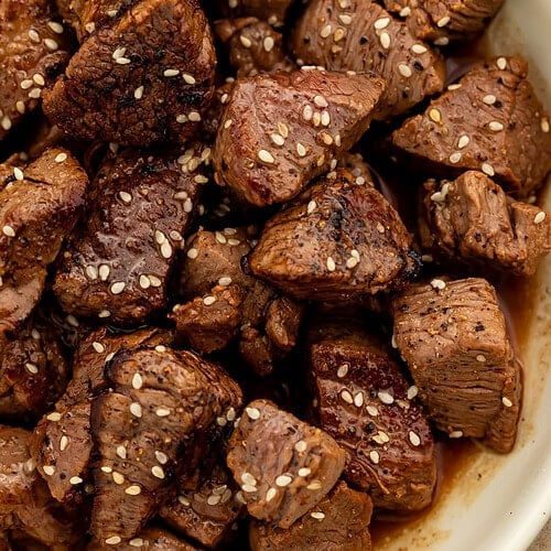 Close up of a bowl of hibachi steak bites scattered with sesame seeds.