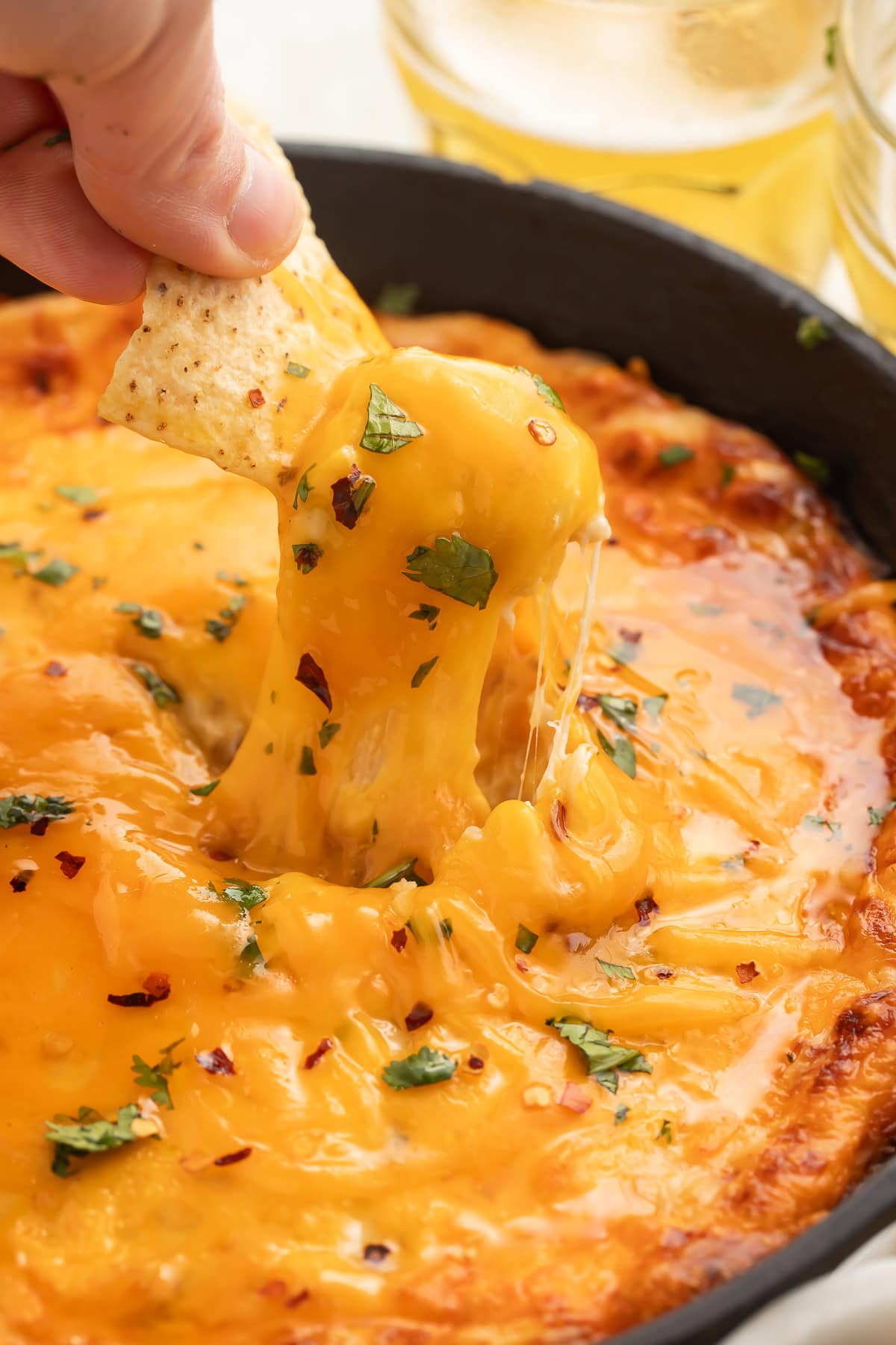 Cheesy dip being scooped from a skillet with a tortilla chip.