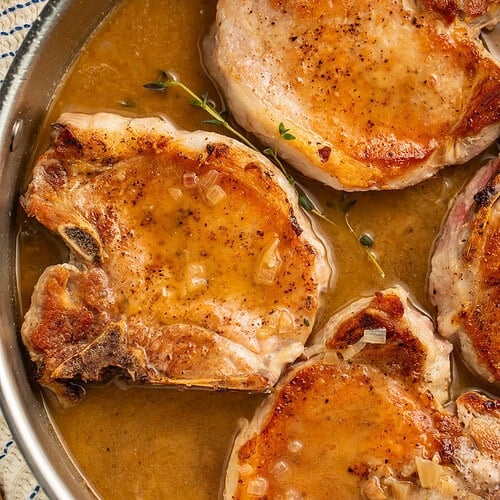 Close up of a pan of seared pork chops sitting in their own pan sauce.