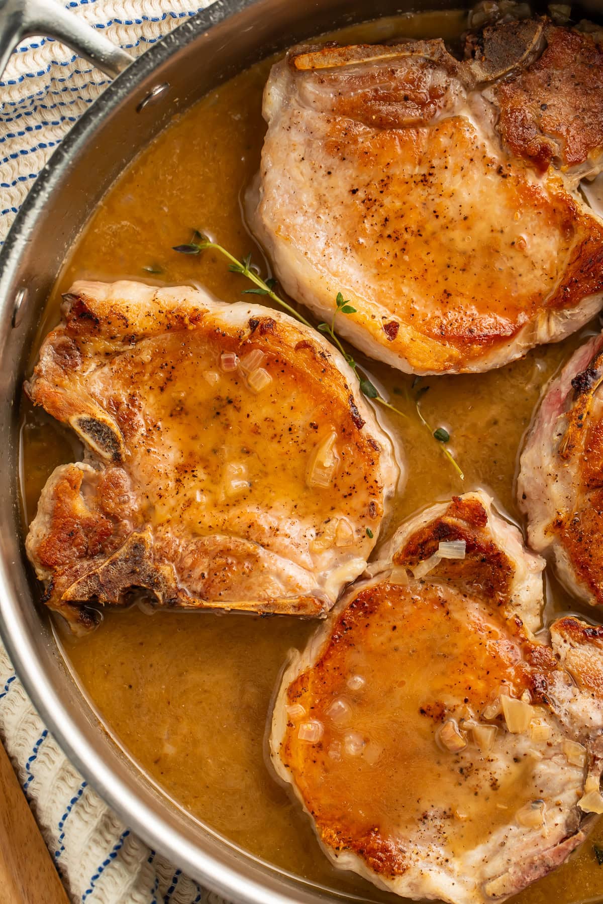 Close up of a pan of seared pork chops sitting in their own pan sauce.