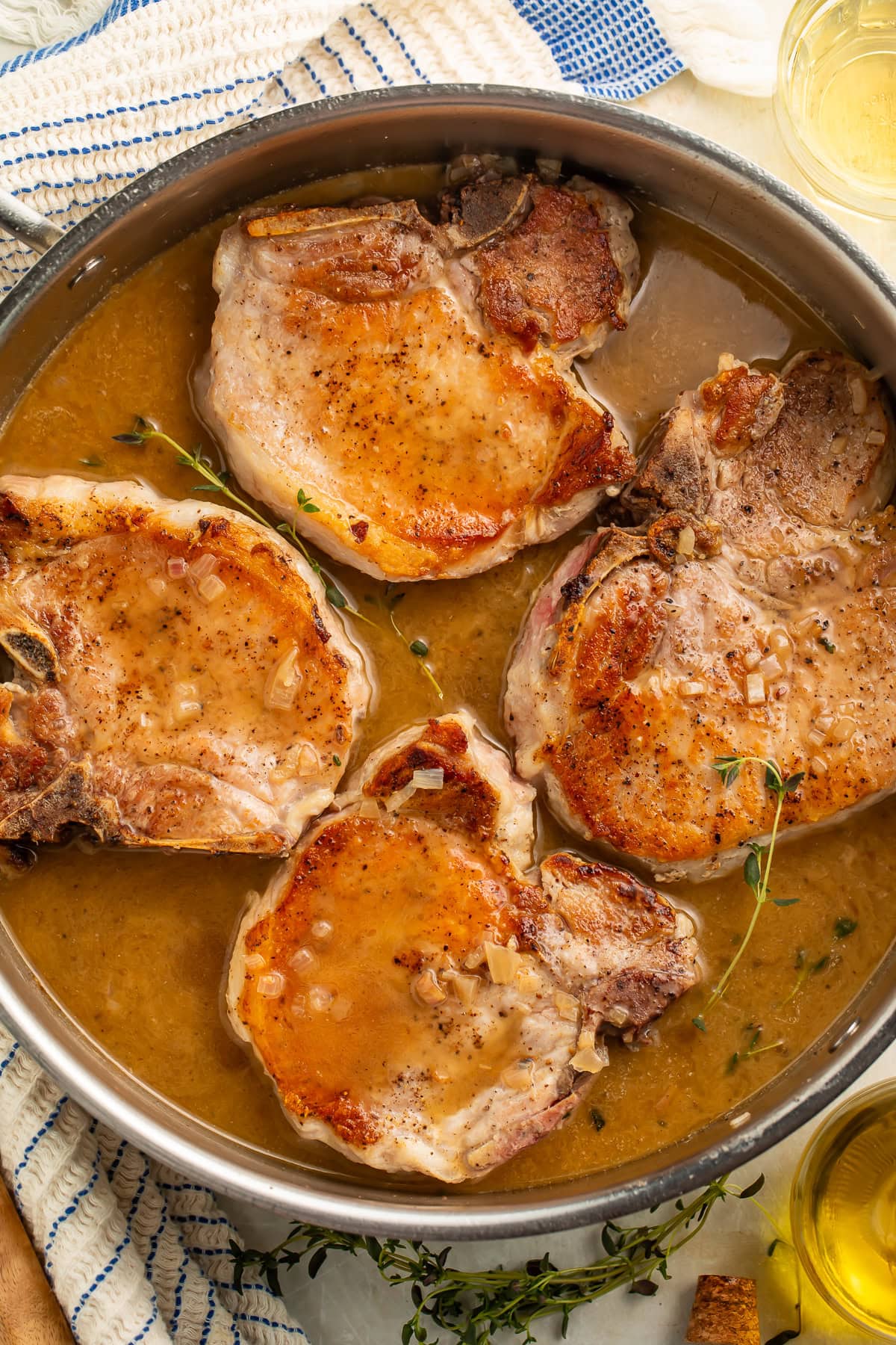 Overhead image of four pork chops in a frying pan with thyme-laced pan sauce.