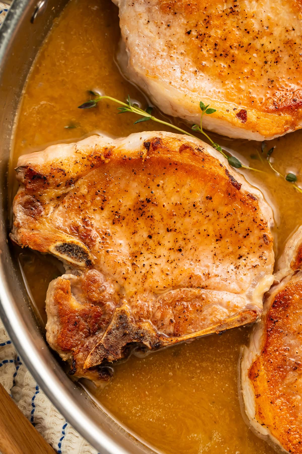 Close up of a seared pork chop in the pan with pan sauce and a fresh thyme sprig.