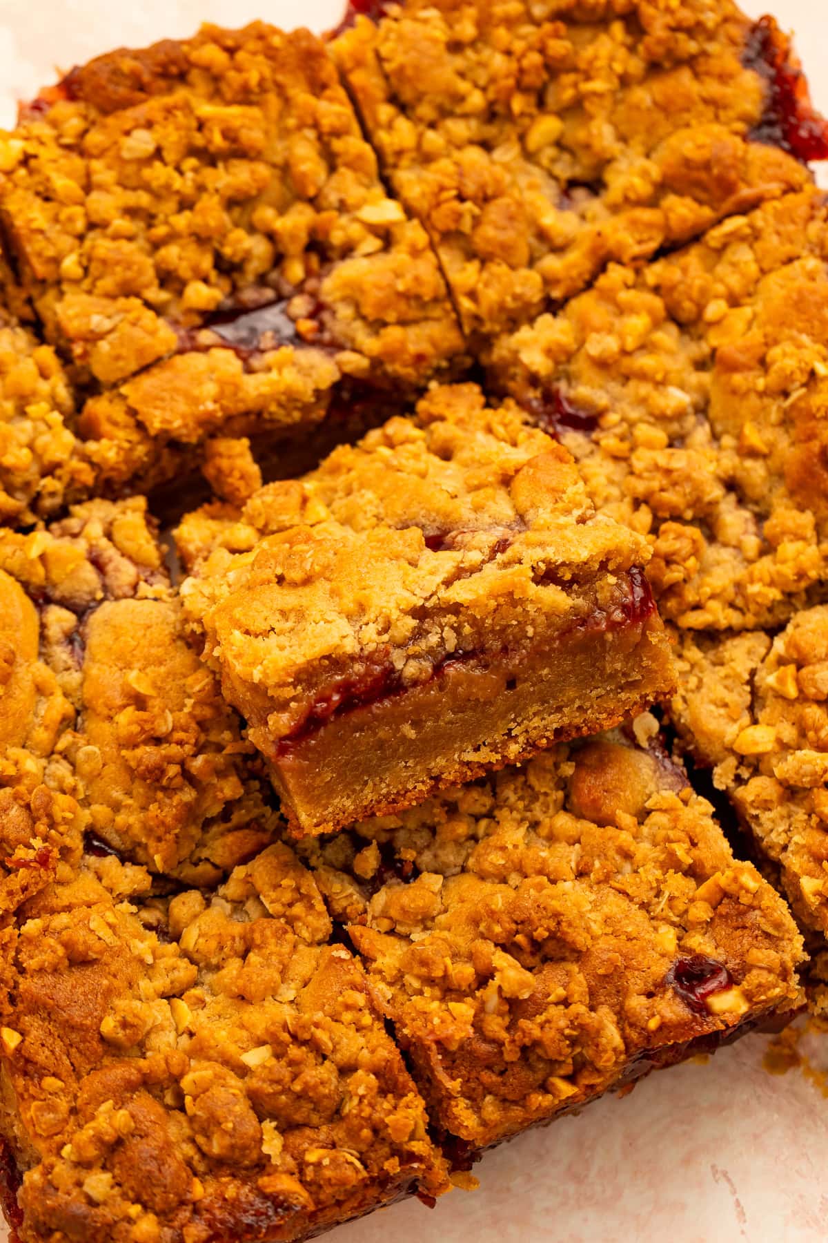 Side-on view of peanut butter and jelly bars as a slab with one bar resting on it's side to show the gooey layers.