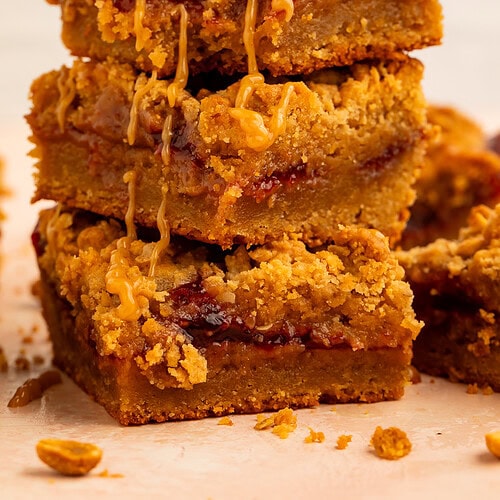 Stack of peanut butter and jelly bars topped with a peanut butter drizzle.