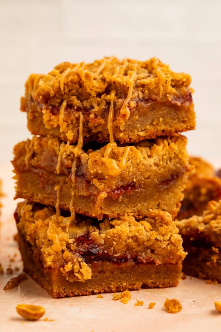 Stack of peanut butter and jelly bars topped with a peanut butter drizzle.
