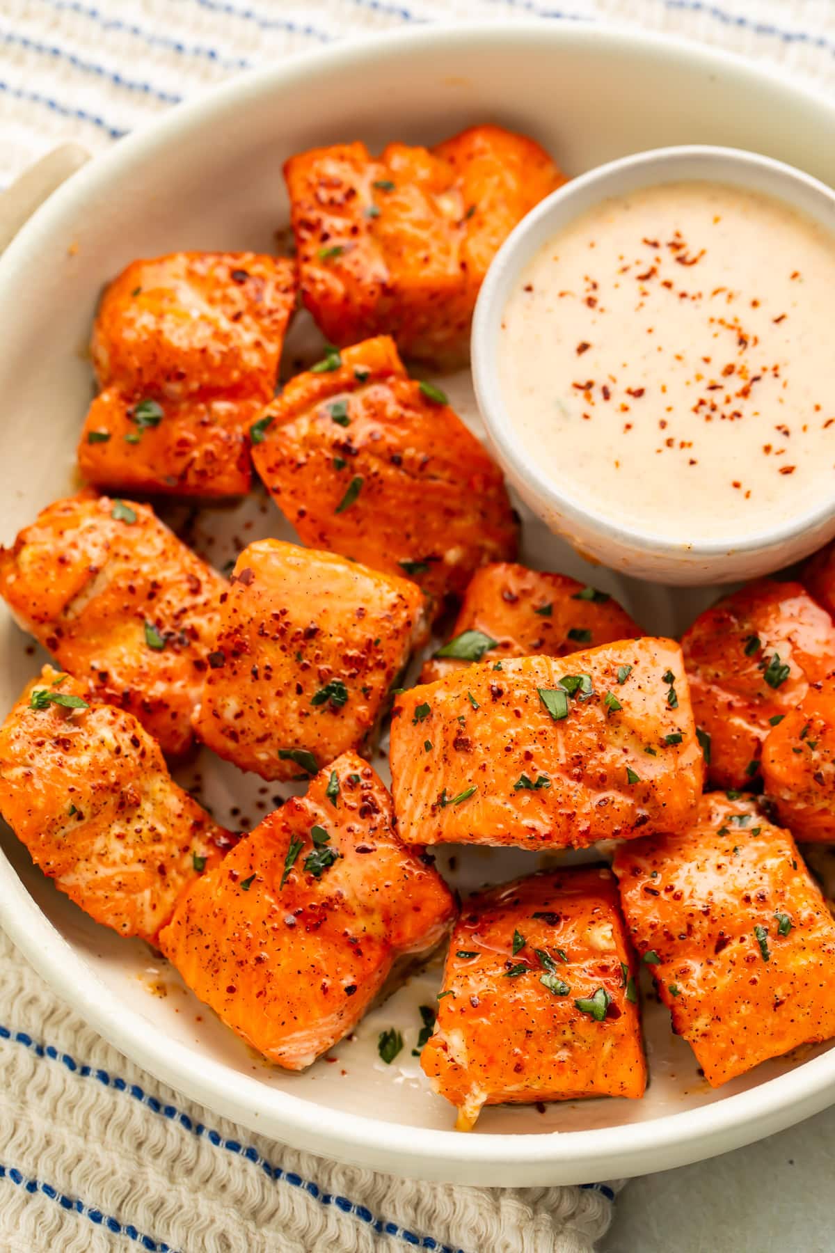 White bowl of salmon bites with a pot of creamy spicy sauce.