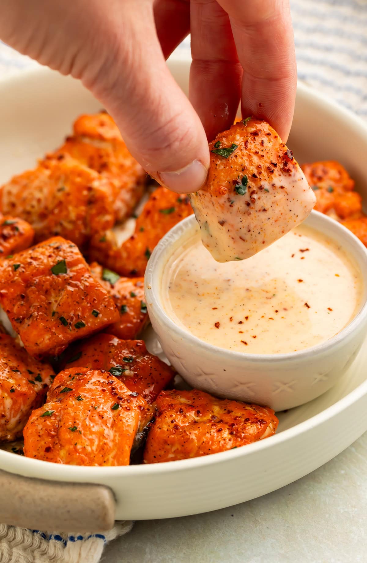 A hand dipping a Cajun honey-glazed salmon bite in a pot of creamy sauce.