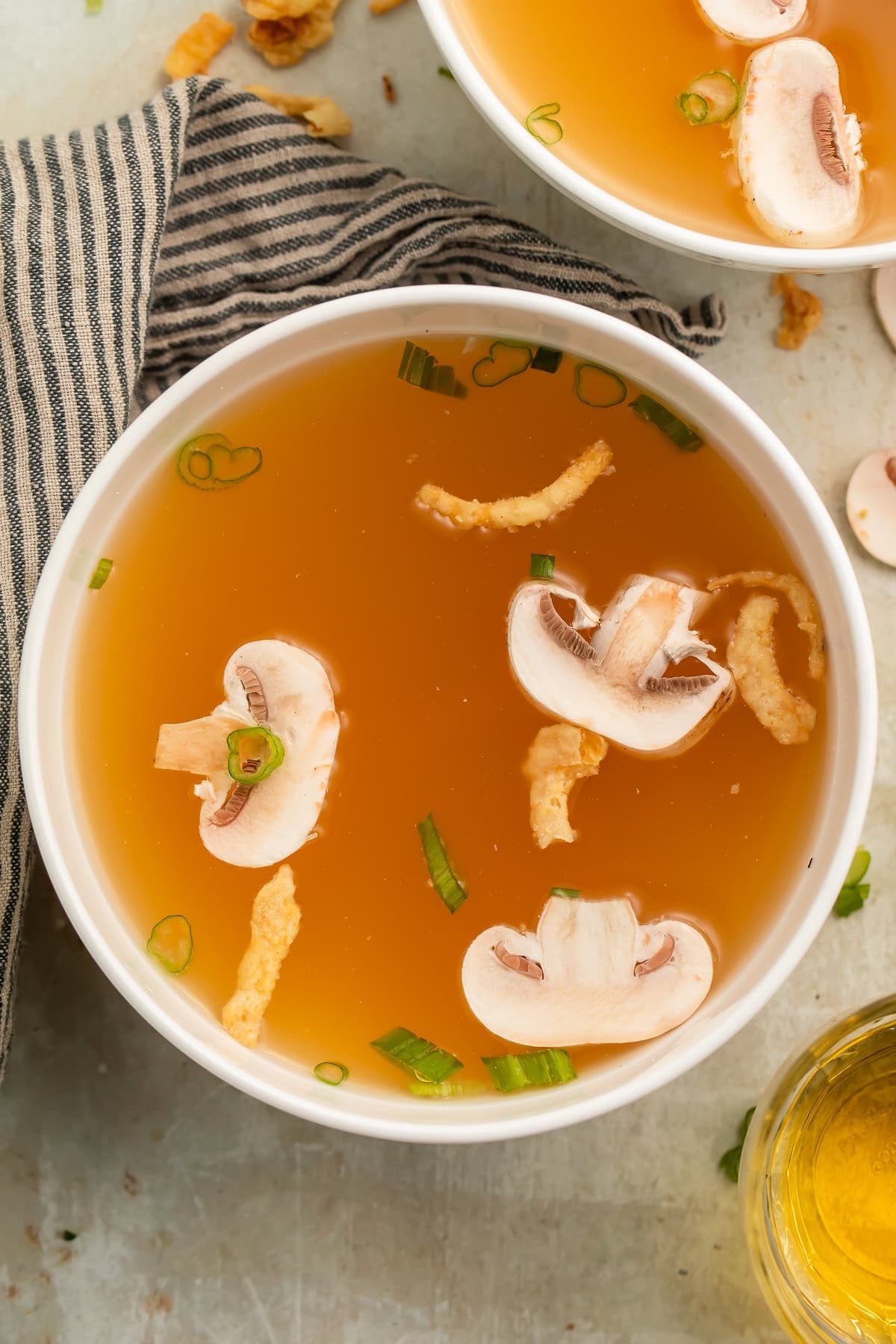 White bowl of clear soup with sliced mushrooms and green onions.