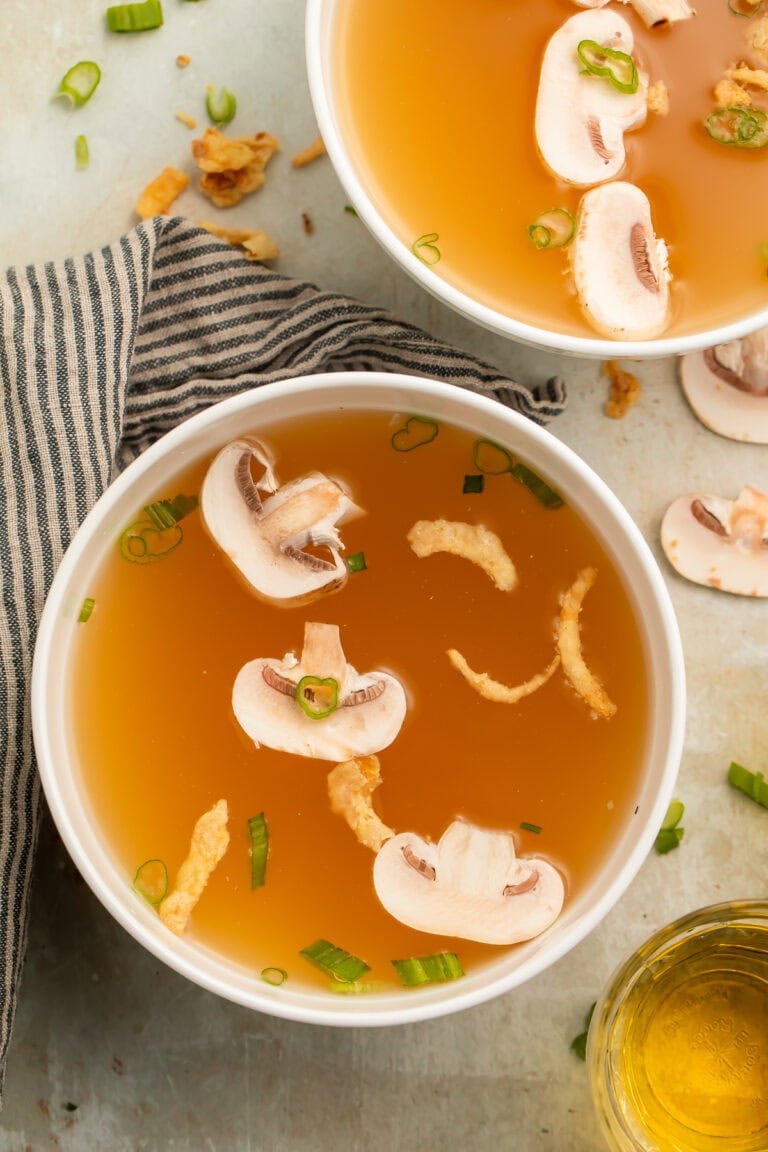 Two bowls of clear soup with sliced mushrooms, sliced green onions and crispy onions.