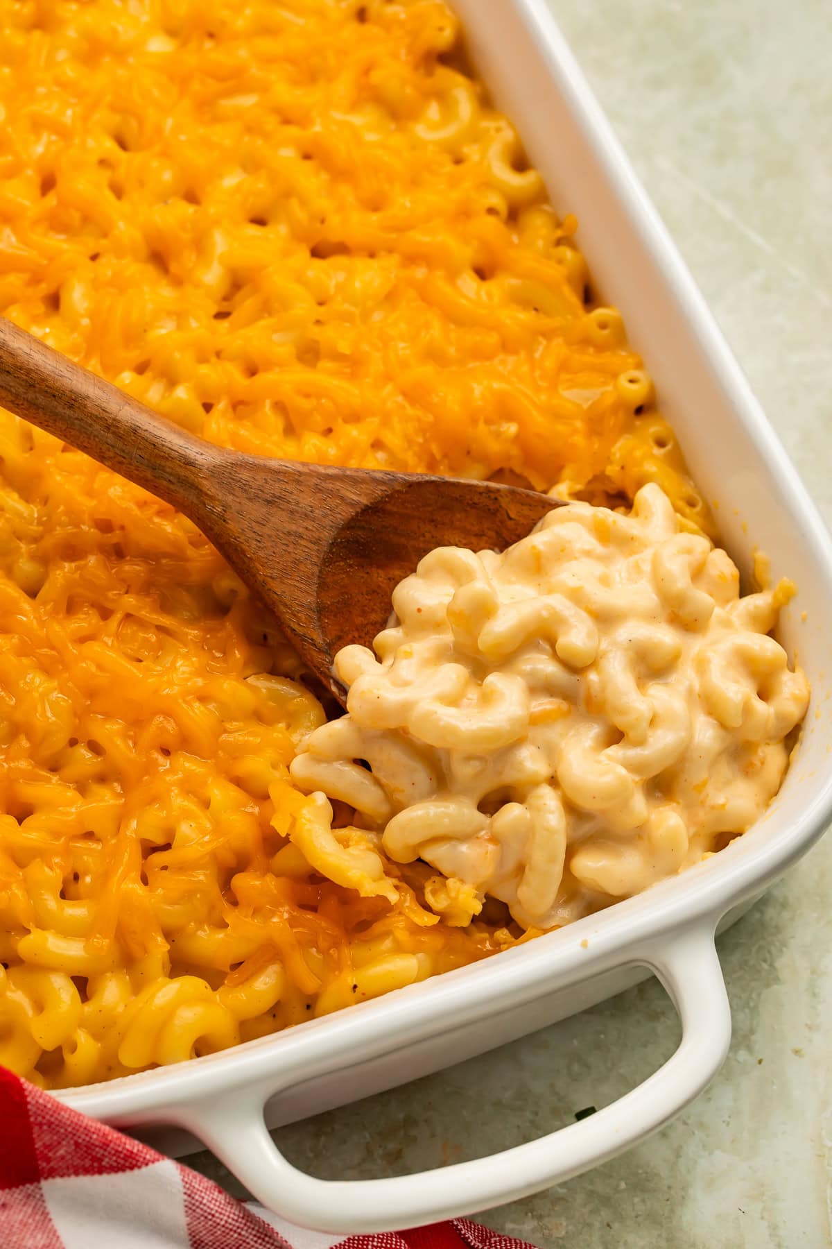 Wooden spoon scooping macaroni and cheese out of the white baking dish.