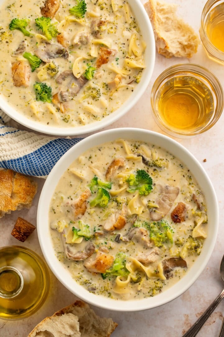Two bowls of chicken divan soup with egg noodles. Glasses of beer are pictured on the side.