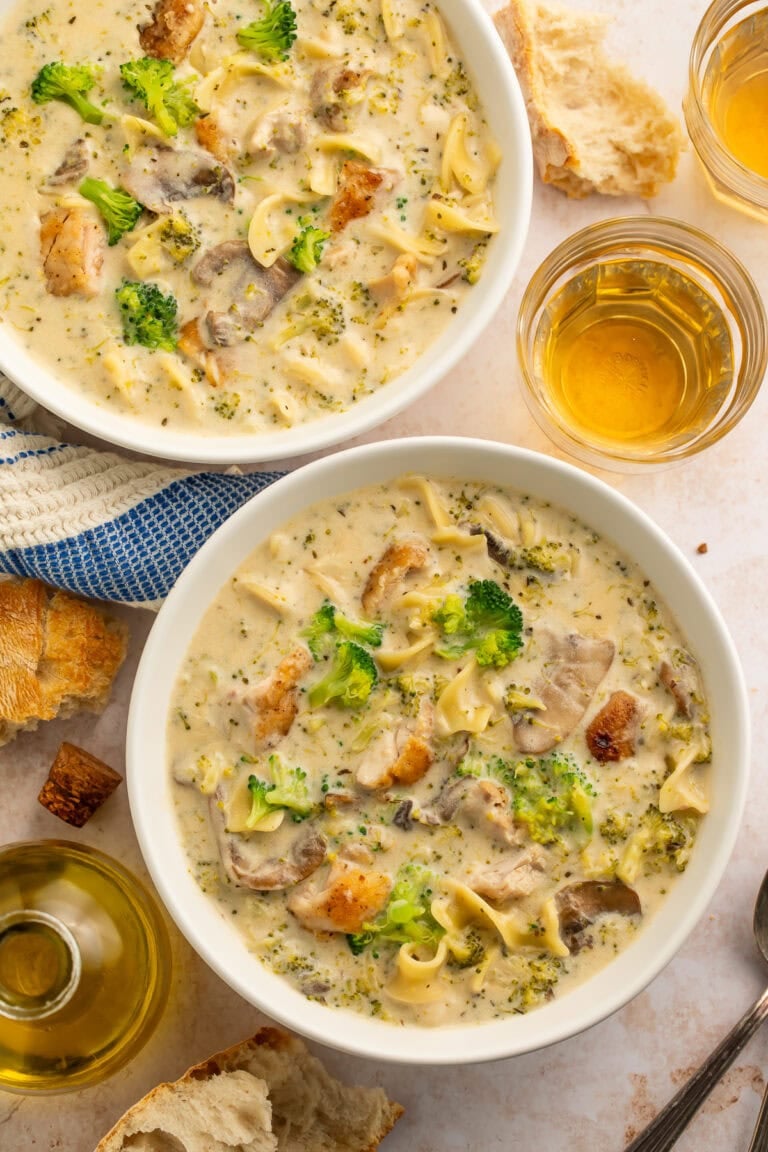 Two bowls of chicken divan soup with egg noodles. Glasses of beer are pictured on the side.