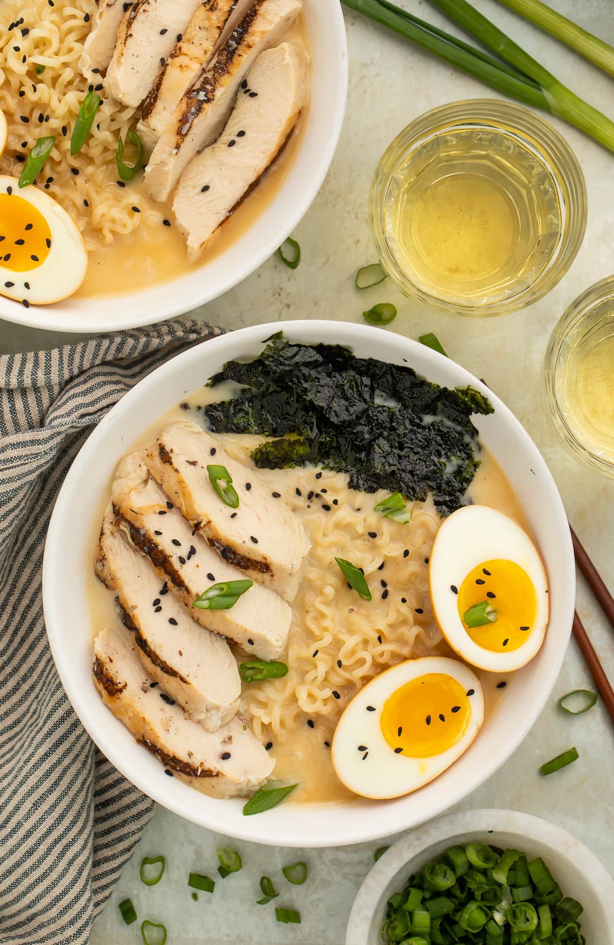 Two bowls of chicken ramen topped with sliced chicken, sesame seeds, green onion, boiled egg and nori.
