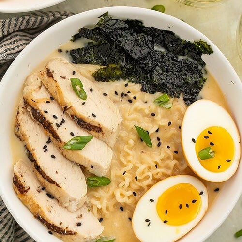 Close up of a bowl of ramen topped with sliced chicken, nori, soft boiled egg, sesame seeds and sliced green onions.