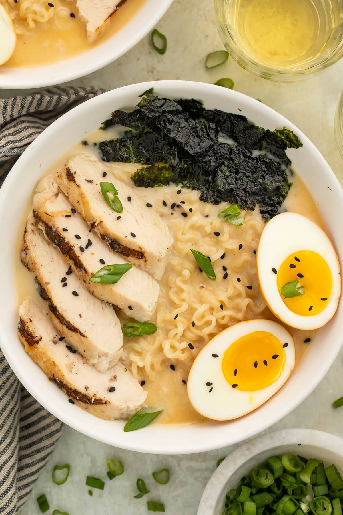 Close up of a bowl of ramen topped with sliced chicken, nori, soft boiled egg, sesame seeds and sliced green onions.