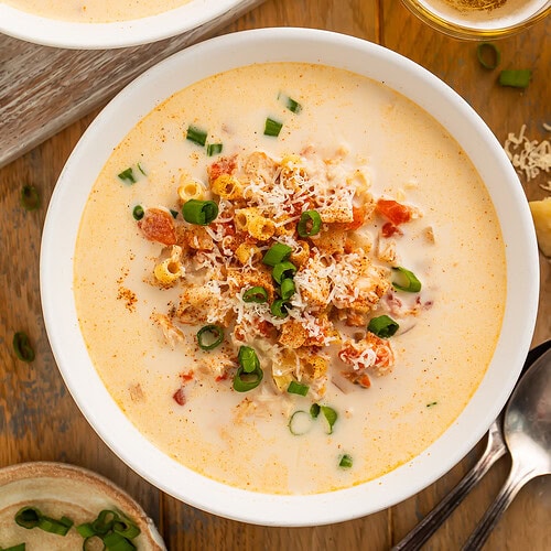Overhead image of two bowls of creamy cajun chicken soup with chunks of tomato, garnished with green onion.