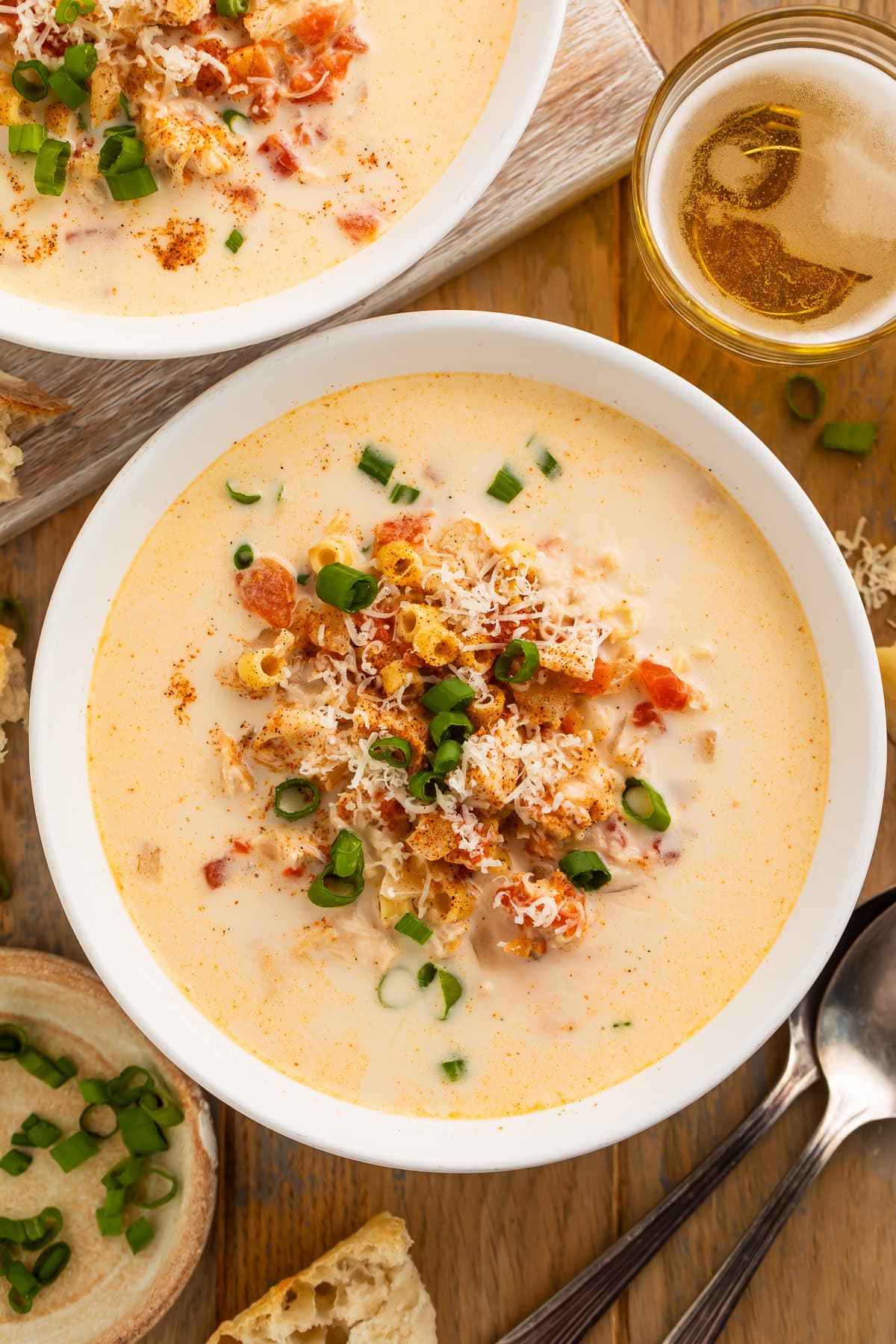 Close up of a bowl of creamy Cajun tomato and chicken soup, garnished with shredded cheese and sliced green onions.