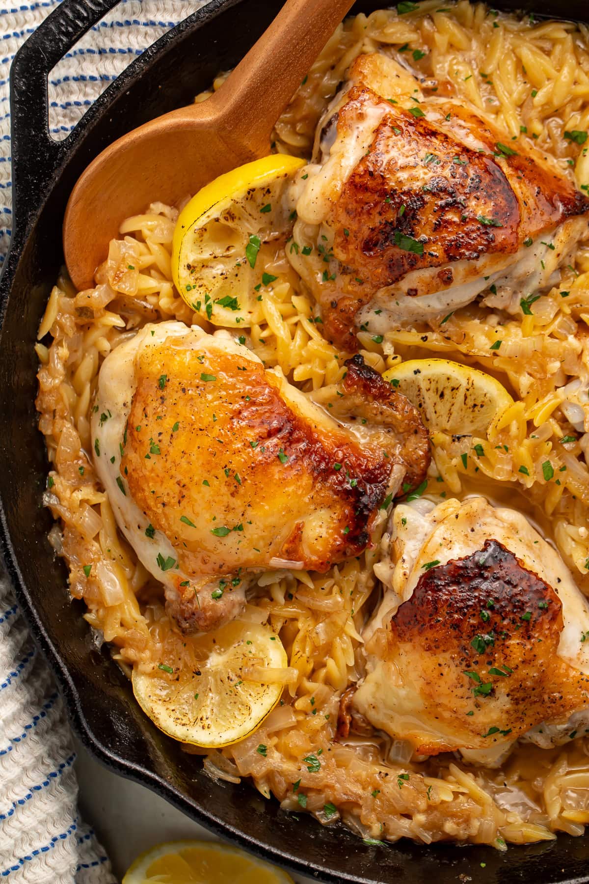 A close up of an orzo skillet with chicken thighs and lemon slices.