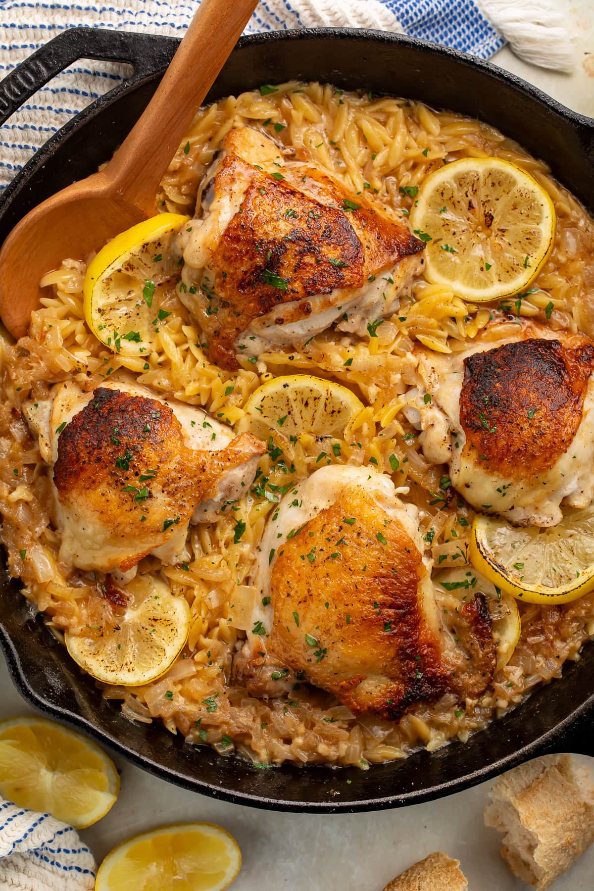 An overhead image of a cast iron skillet of garlic butter orzo with chicken thighs and fresh lemon slices.