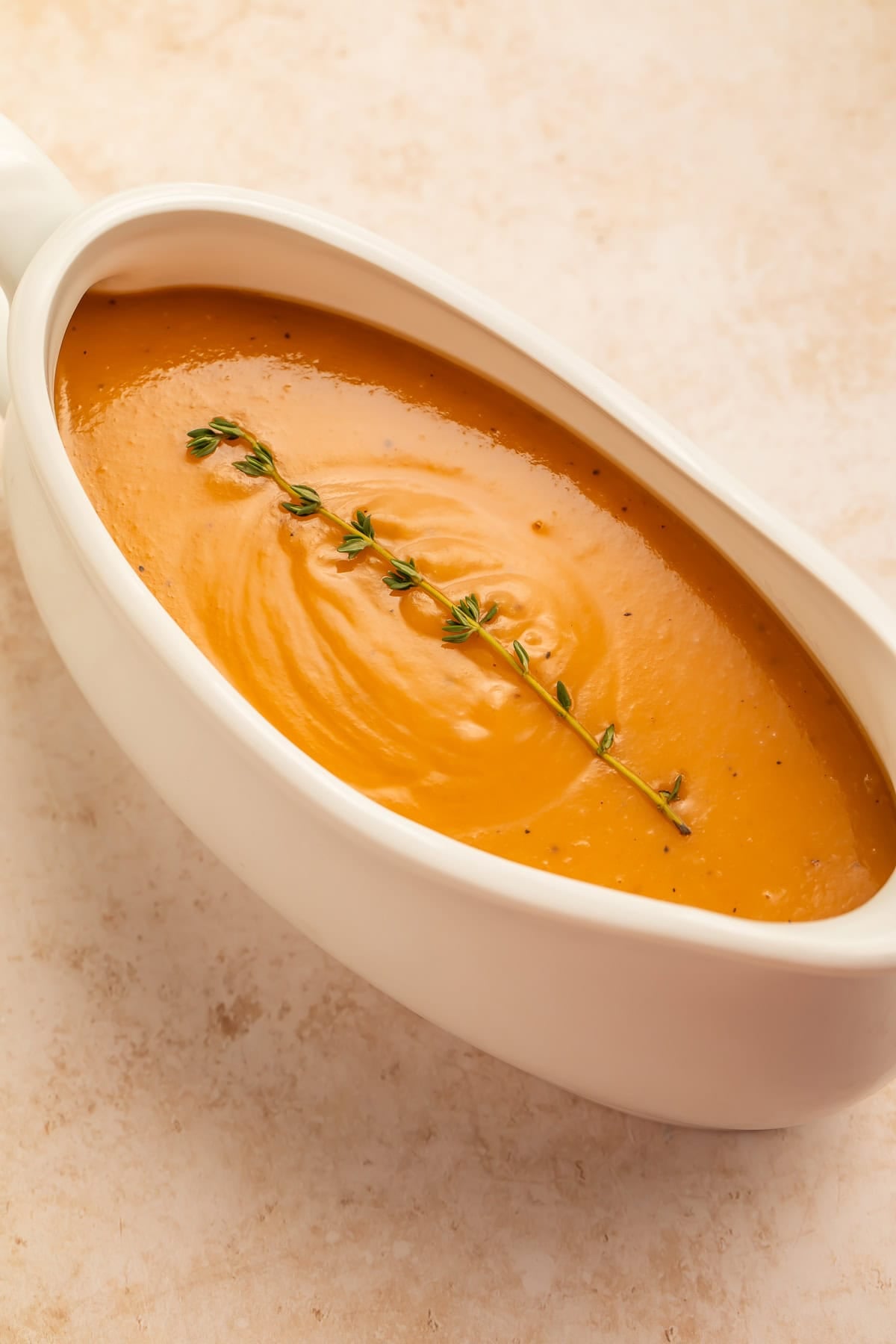 Turkey gravy in a white gravy boat garnished with a single fresh thyme sprig.