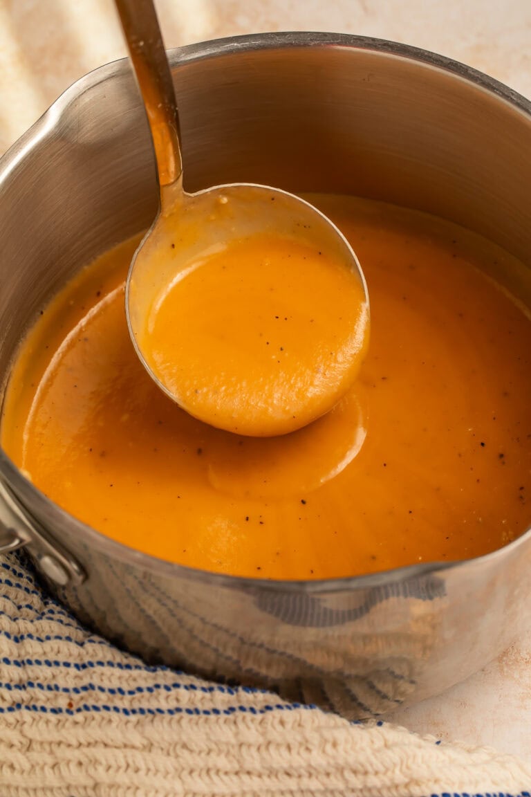 Ladle lifting gravy out of a cooking pot.