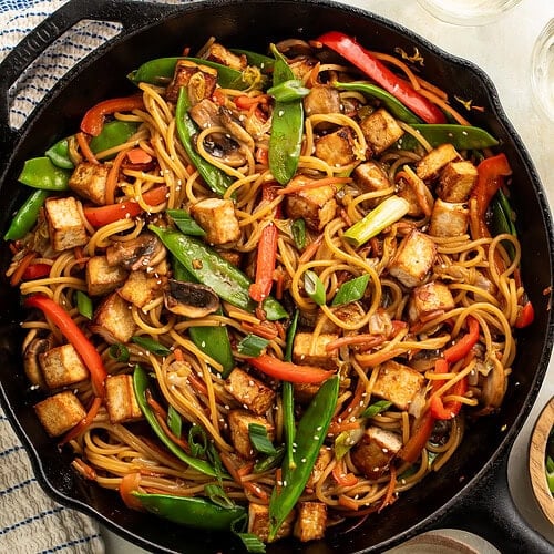 Cast iron skillet of le mein vegetable noodles with cubes of crispy tofu.