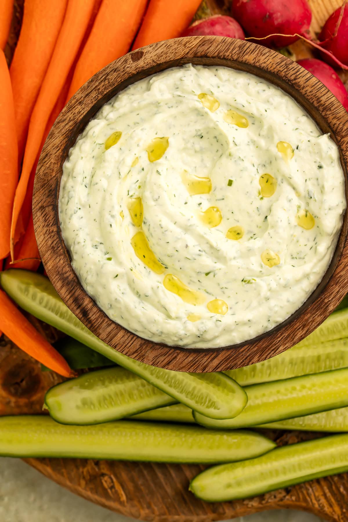 Close up of a wooden bowl of herby whipped cream cheese dip surrounded by crudites.