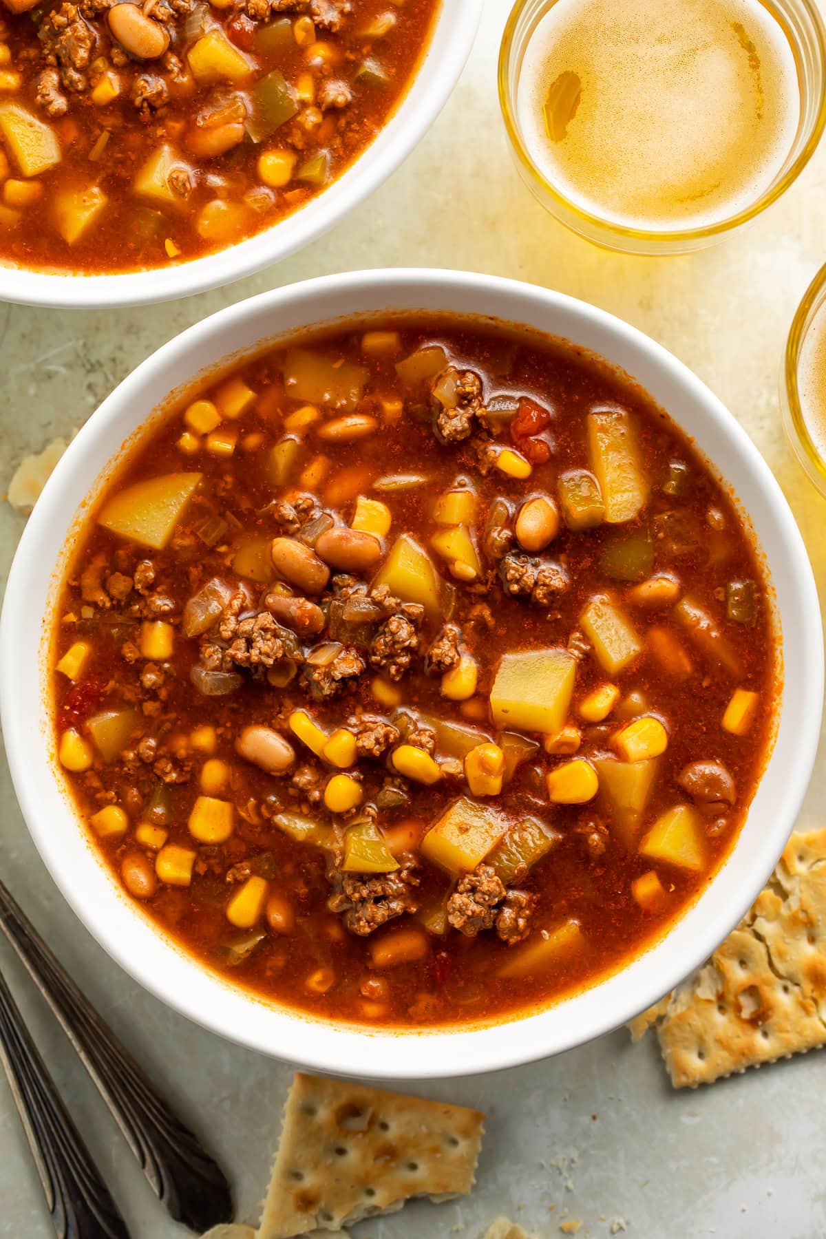 White bowls of cowboy soup with cups of beer and crackers on the side.