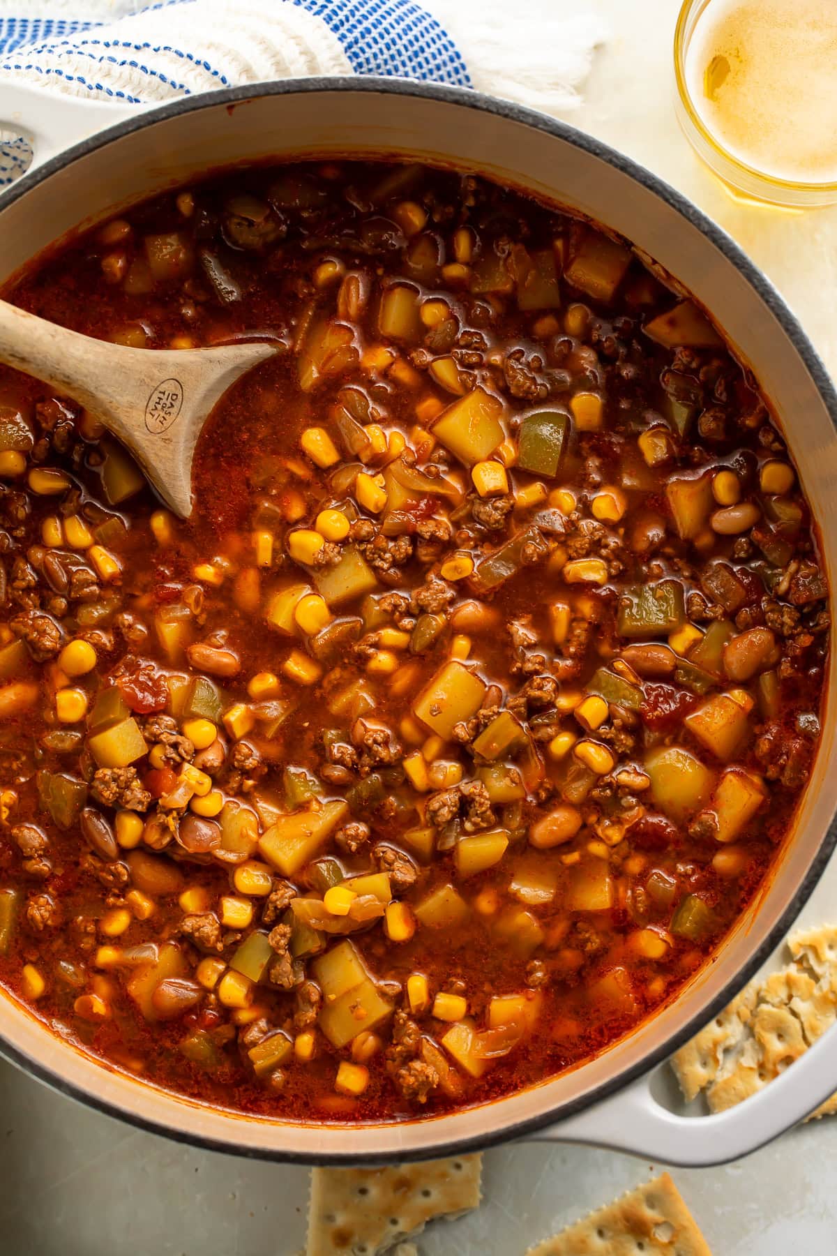 Pot of Cowboy soup with beef, corn and beans with a wooden spoon resting in it.