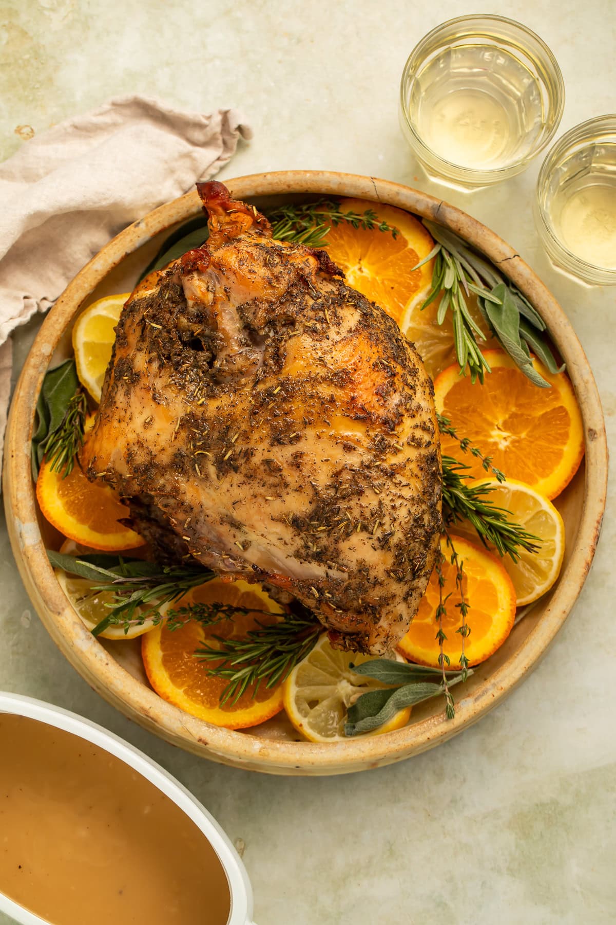 Whole herbed turkey bread on a platter of sliced oranges and woody herbs.