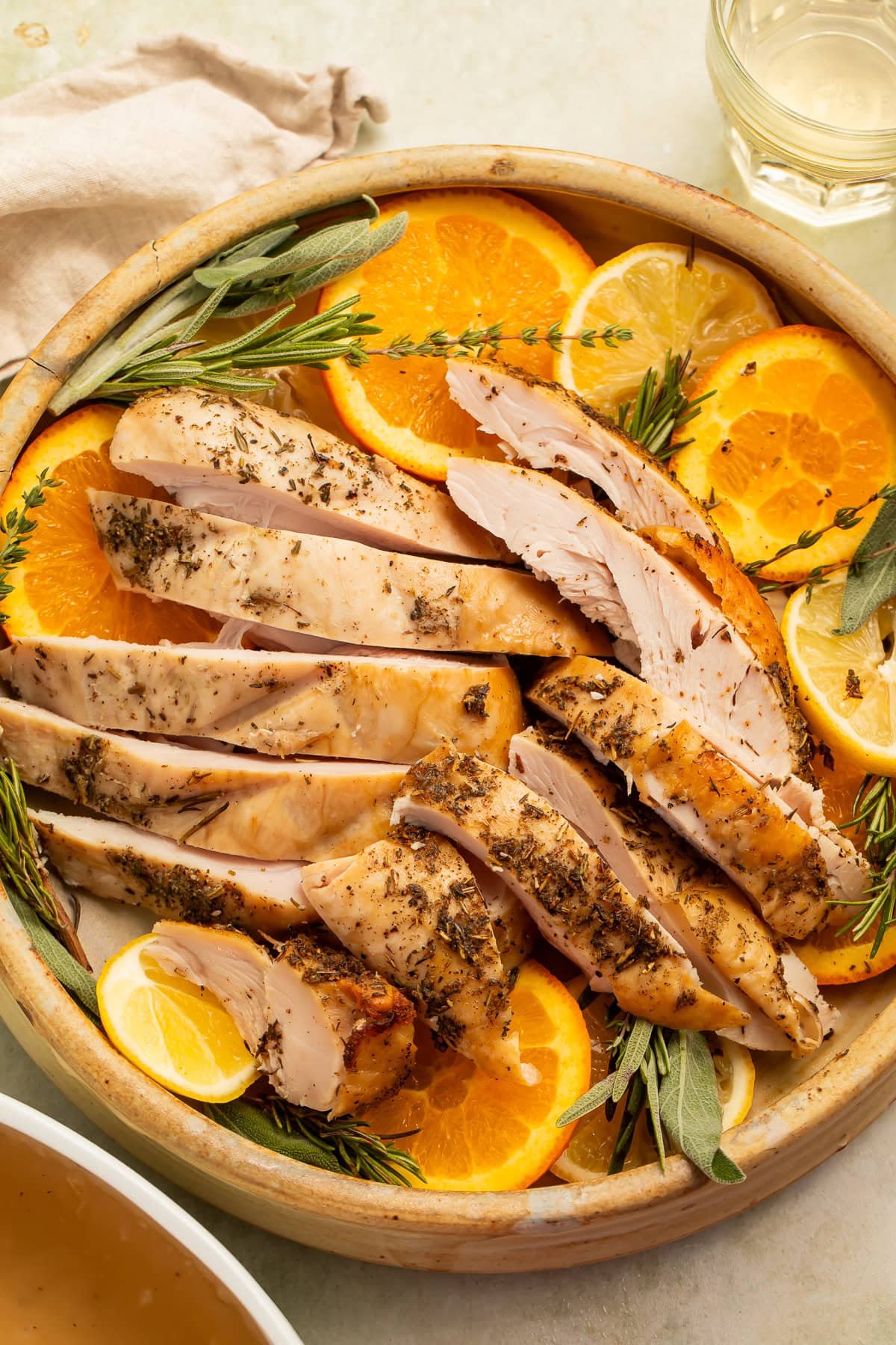 Sliced turkey breast on a platter with sliced oranges and woody herbs.