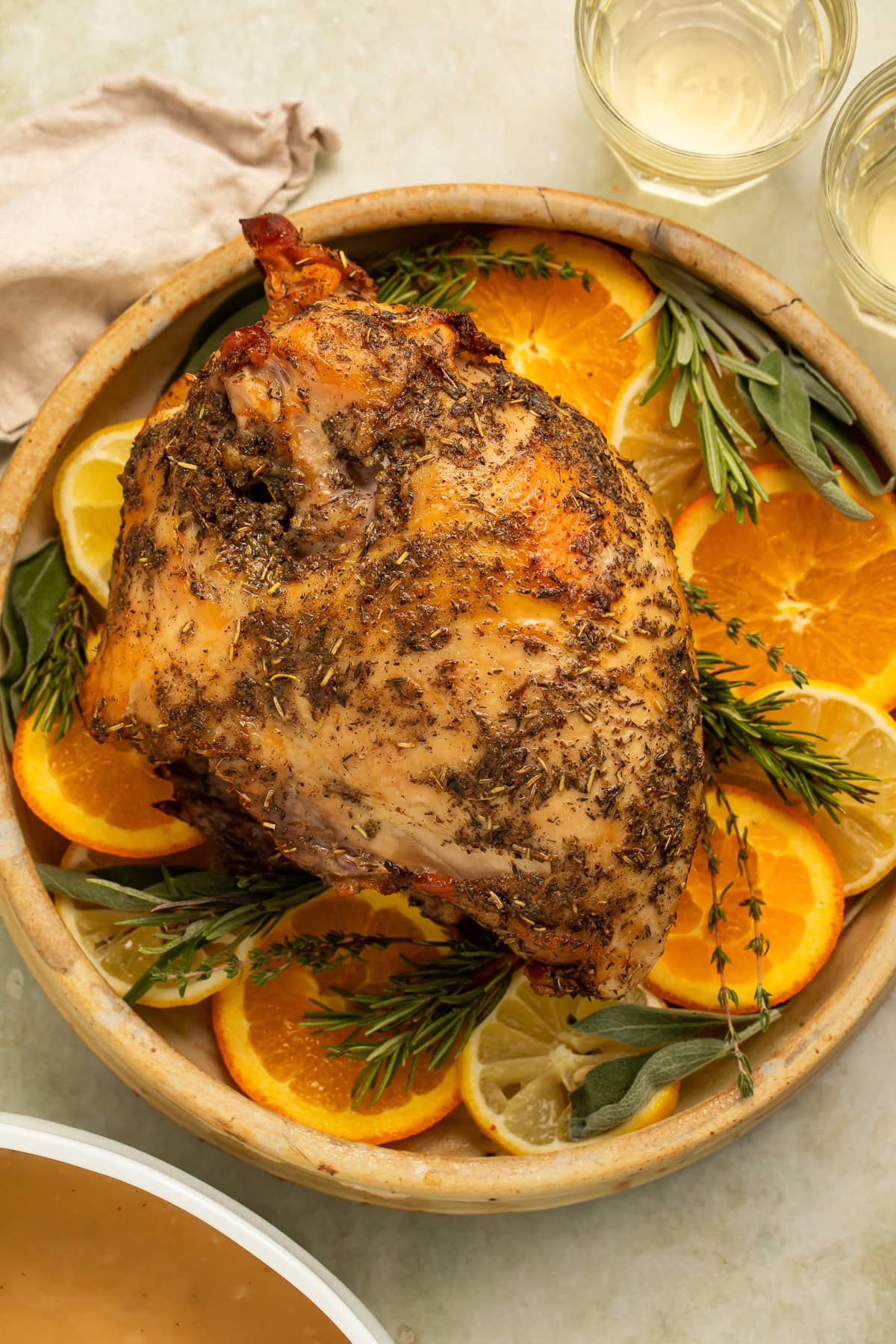 Whole roasted turkey breast on a serving platter with sliced oranges and woody herbs.