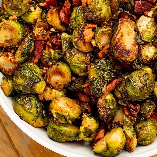 Close up of a white dish of glazed brussels sprouts with pecan and bacon.