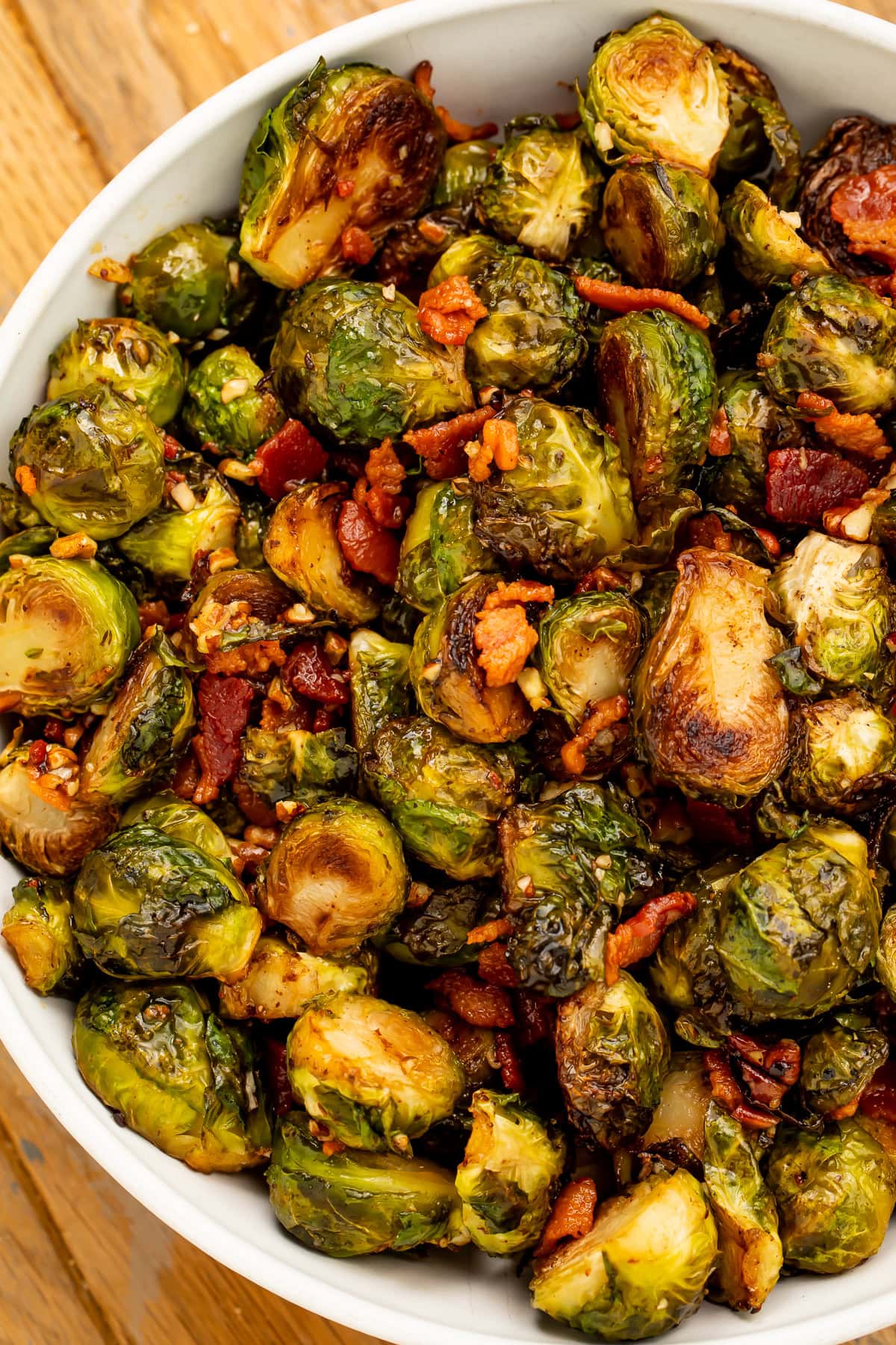 Close up of a white dish of glazed brussels sprouts with pecan and bacon.