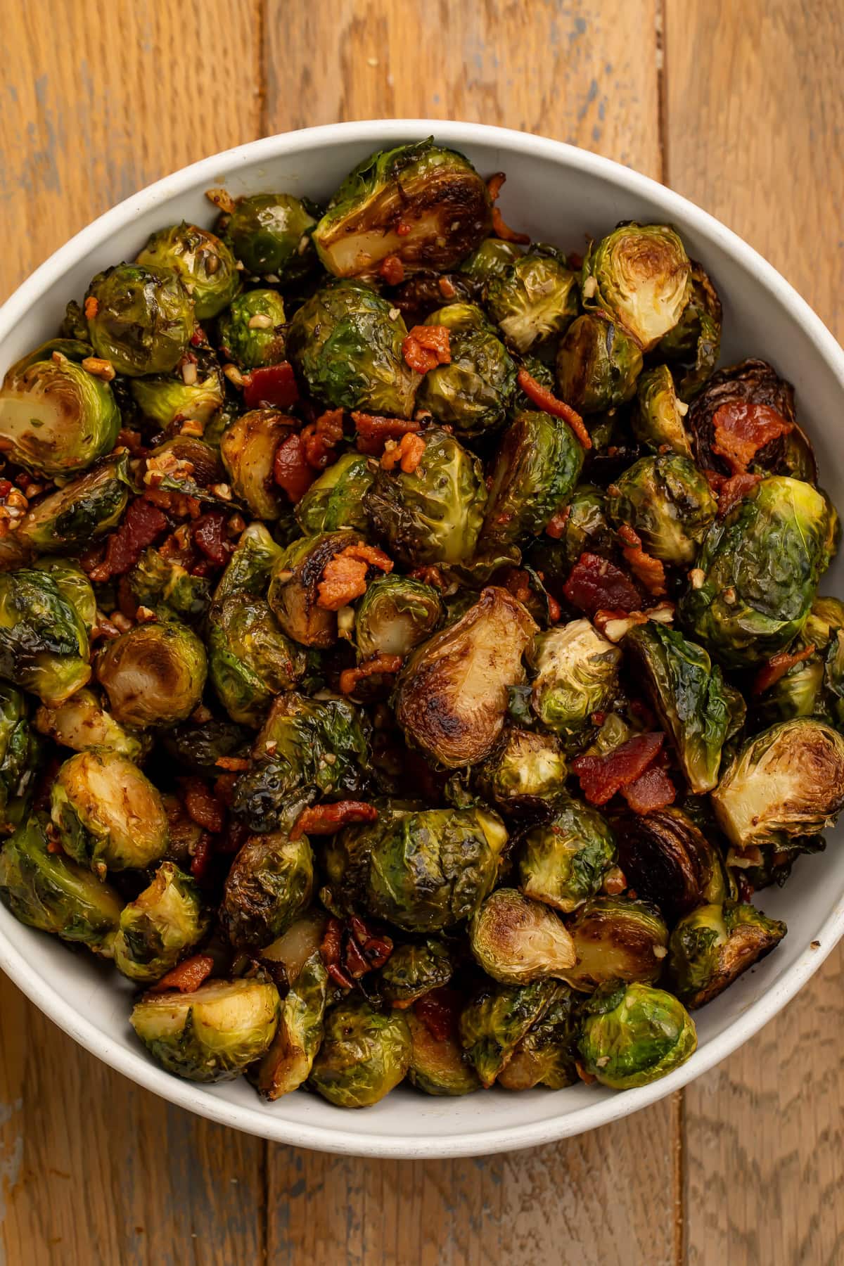 White bowl of roasted glazed brussels sprouts with chopped pecans and bacon pieces.