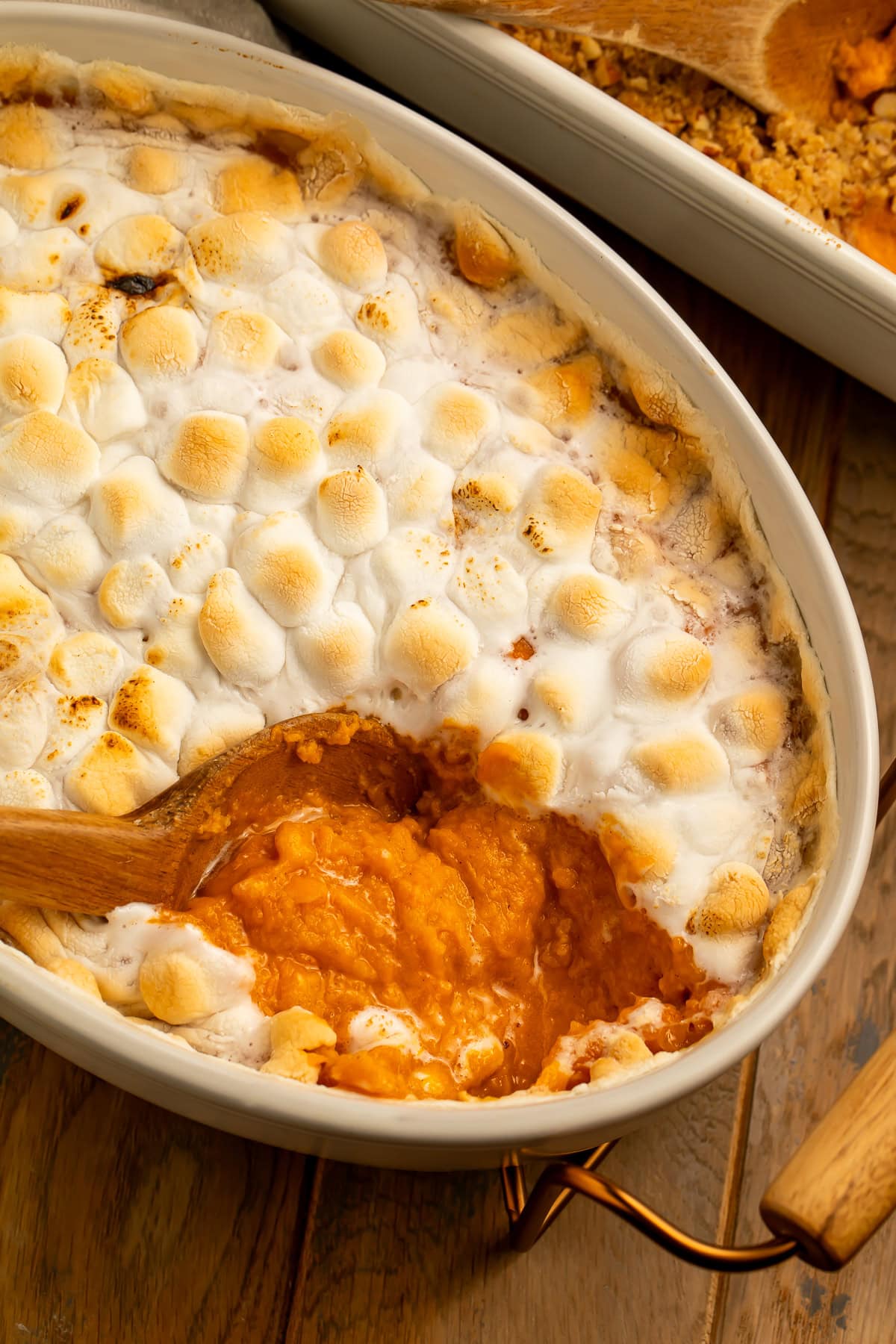 Close up of a sweet potato casserole topped with mini marshmallows. There is a spoonful missing to show the sweet potato layer.