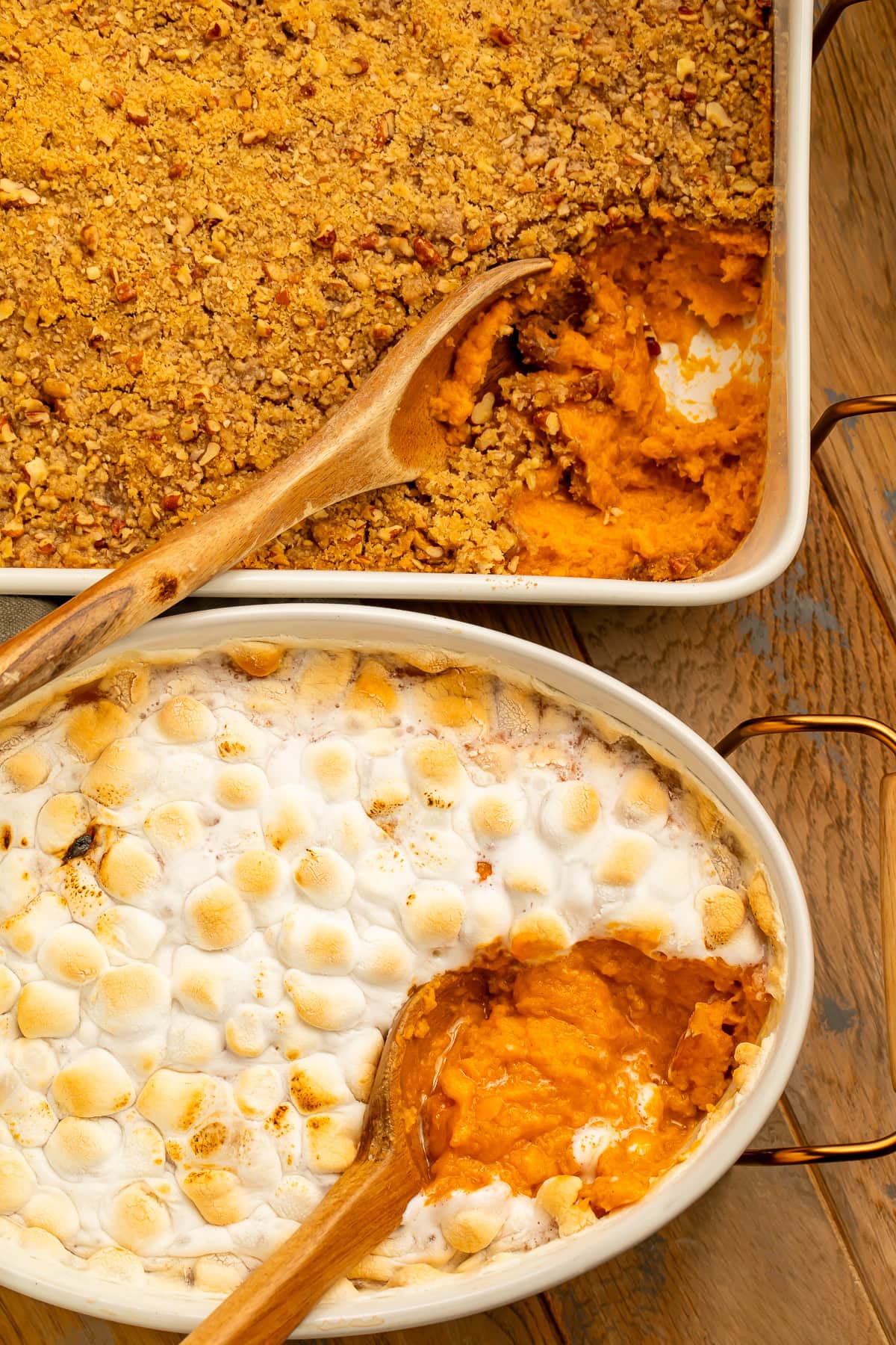 Two sweet potato casseroles pictured overhead with a spoonful missing to show the sweet potato layer. One is topped with streusel and the other mini marshmallows.