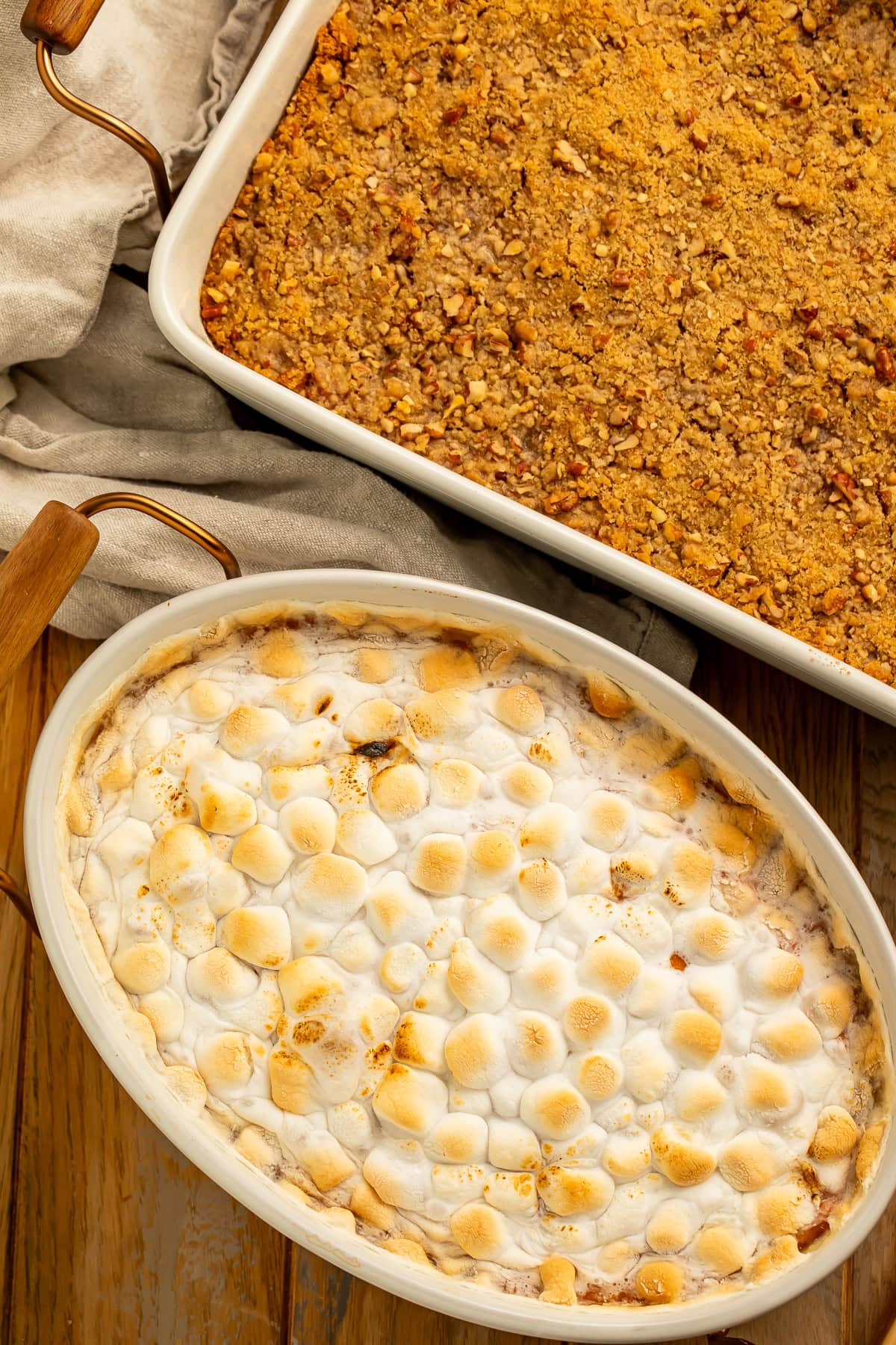 Two baked sweet potato casseroles, one topped with pecan streusel one the other with melted marshmallows.